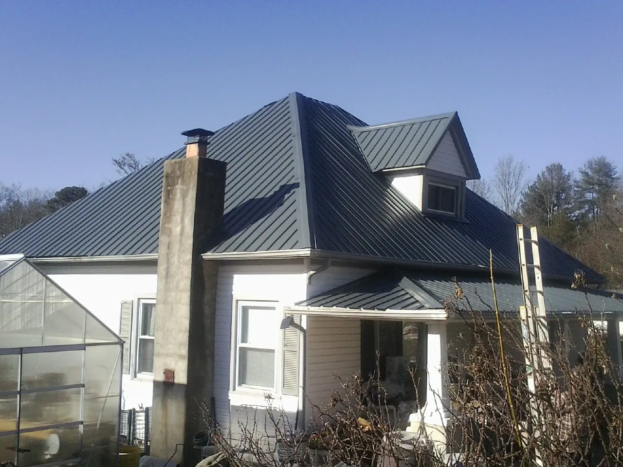 Dark blue standing seam metal roof on a white farmhouse with dormer — Slate & Tile Roof Repair by Roofing Brothers in North Webster