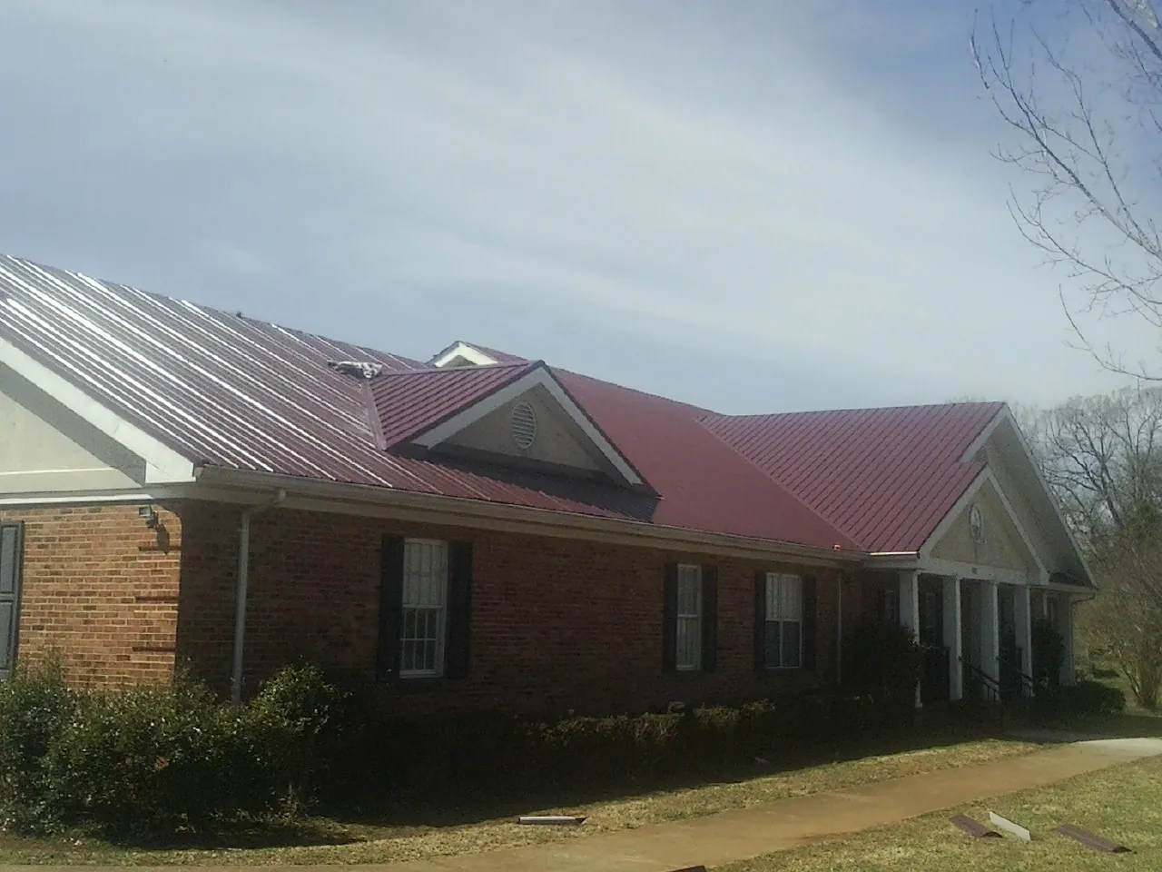 Red metal roof with gabled entries on a long brick building, from a Hail Damage Roof Repair job in North Webster