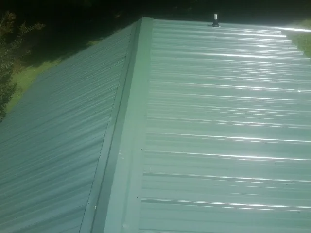 New green metal panels meeting at the ridge of a roof — Flat Roof Repair work by our crew in North Webster