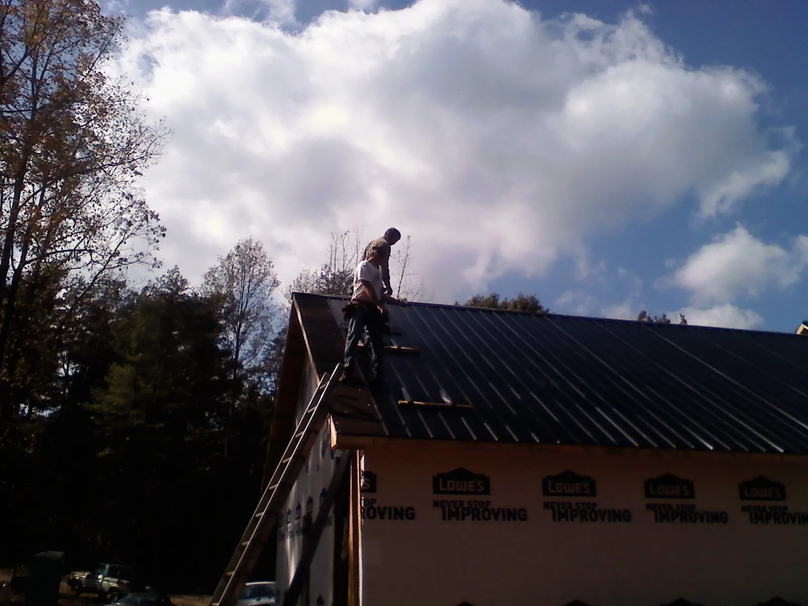 Roofer fastening dark metal panels high against a cloudy sky, from a Roof Inspection job in North Webster