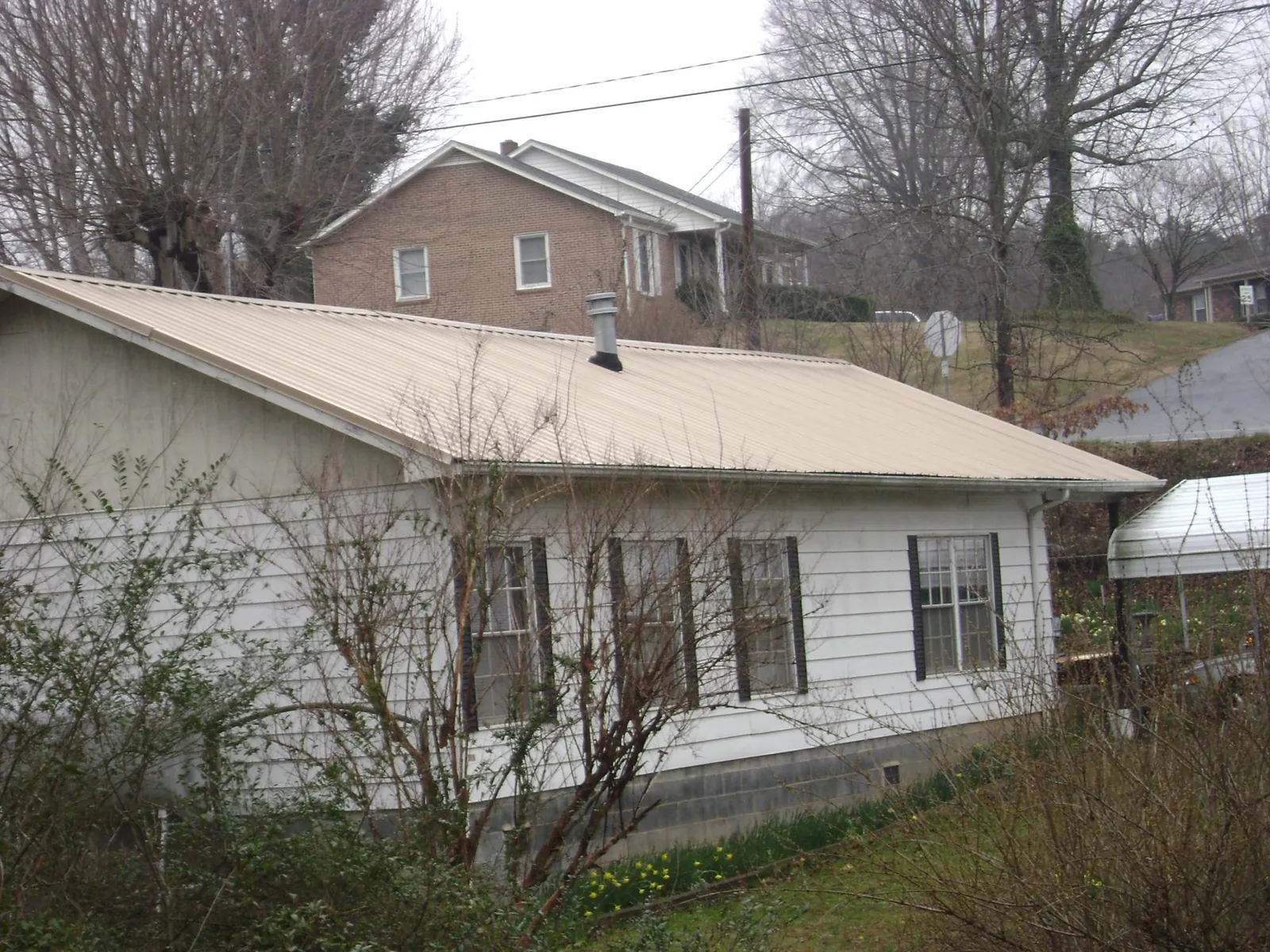 Tan metal roof on a white sided house set into a hillside in North Webster