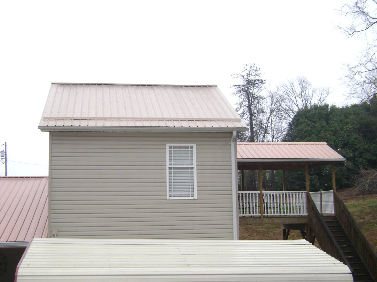 Tan metal roofs on a two story addition and attached porch, from a Roof Replacement job in North Webster